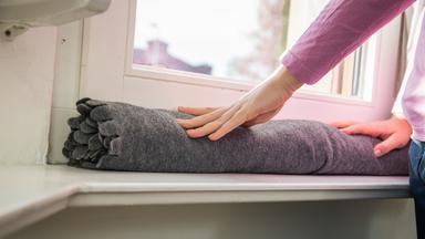 Eine Frau legt eine zusammengerollte Wolldecke vor ihr Fenster.