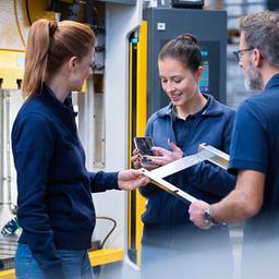 Mitarbeiterinnen und ein Mitarbeiter der Metallindustrie sind während eines Gesprächs am Arbeitsplatz zu sehen.