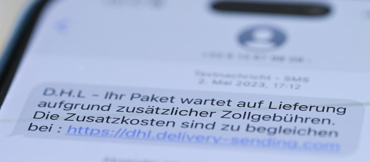 Auf einem Smartphone ist eine Betrugs-SMS zu lesen, in der Kriminelle ein Paket ankündigen und dafür Zollgebühren einfordern.