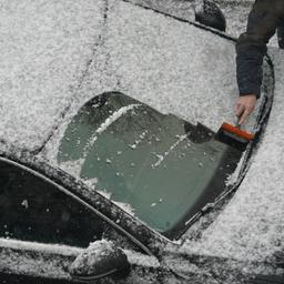 Ein Mann befreit die Windschutzscheibe seines Fahrzeugs vom Neuschnee.