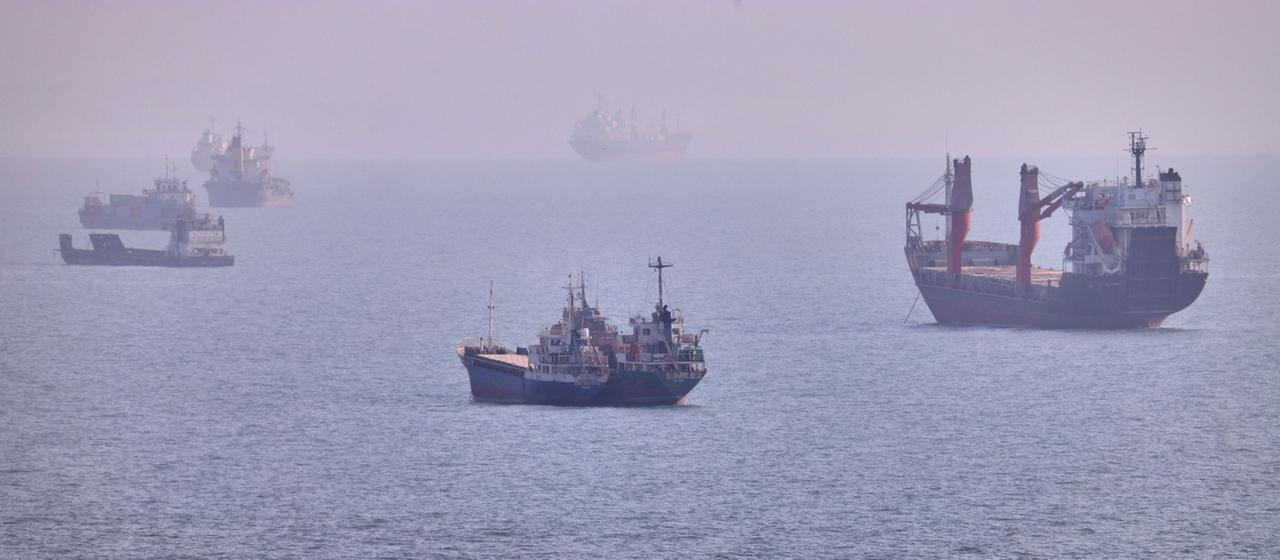 Ein kleines Boot segelt an Frachtschiffen vorbei, die in der Straße von Hormus vor Bandar Abbas im Iran vor Anker liegen.