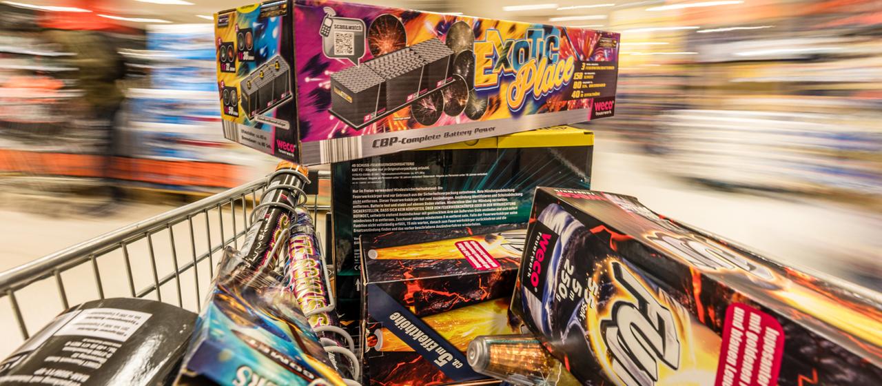Ein Einkaufswagen mit Feuerwerk wird durch einen Supermarkt geschoben.