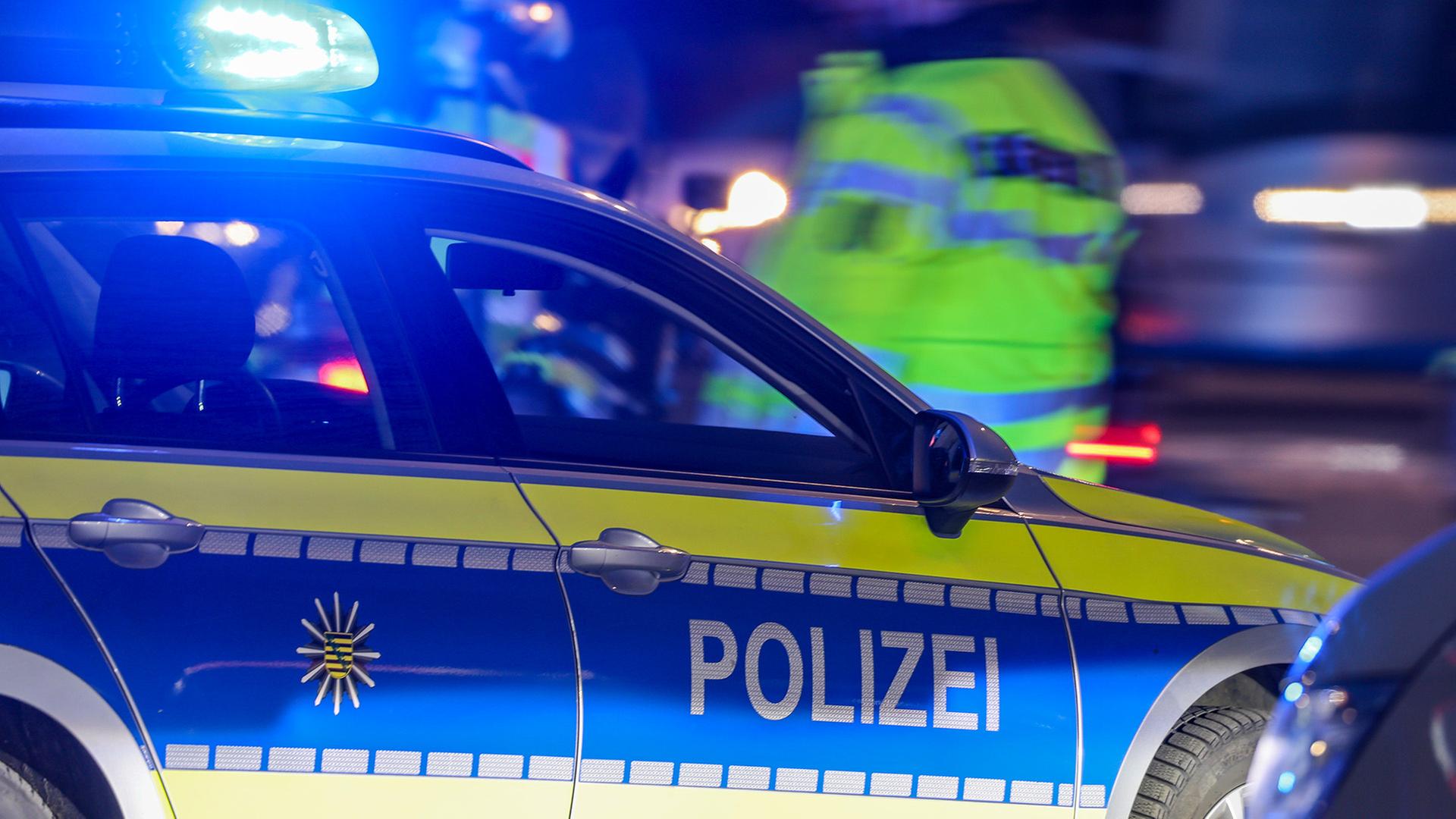 Symbolbild: Ein Polizist steht nachts neben einem Polizeifahrzeug. (Quelle: dpa/Jan Woitas) | dpa/Jan Woitas
