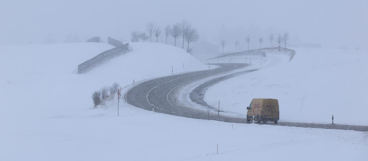 Ein Lieferwagen ist auf einer winterlichen Landstraße unterwegs.
