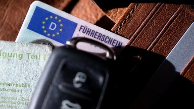 Ein Führerschein, ein Autoschlüssel und eine Zulassungsbescheinigung liegen auf einem Portemonnaie.