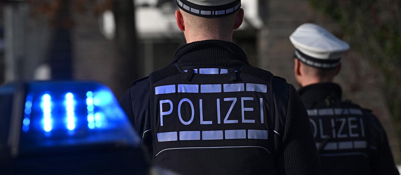 Polizisten die vor einem Blaulicht stehen.