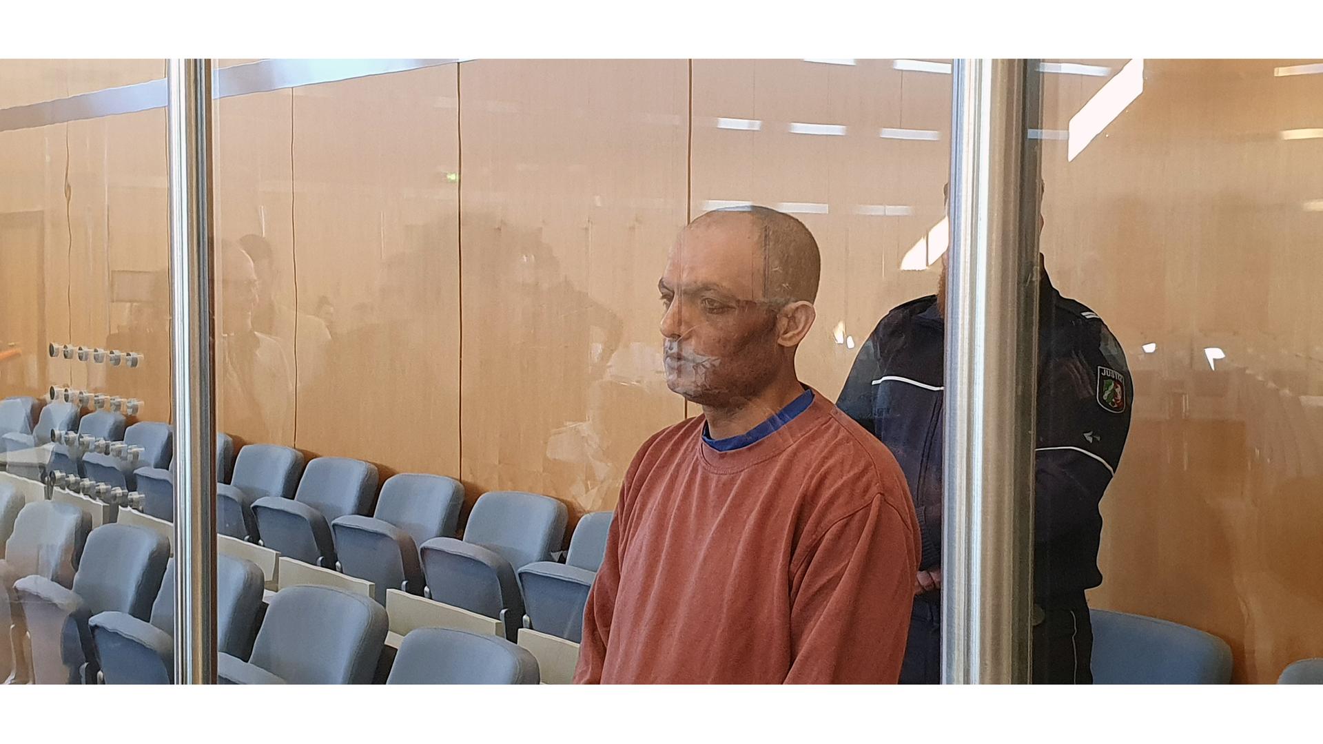 Der Angeklagte steht im Gerichtssaal. Hinter einer Säule steht zur Bewachung ein Wächter. | Martin Hoeke/WDR