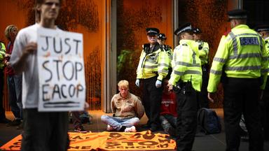 Die Polizei in London steht neben einem Umweltaktivist, der sitzend auf dem Boden protestiert.