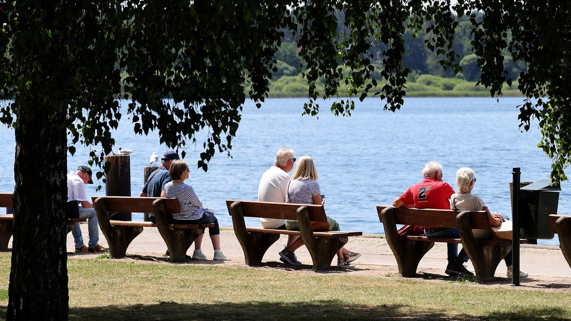 Seniorinnen sitzen bei sommerlichem Wetter auf Bänken am Ufer der Müritz. | picture alliance/dpa