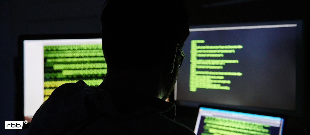 Symbolbild: Ein Mann sitzt vor drei Bildschirmen mit Text (Quelle: picture alliance/dpa/A.Riedl)