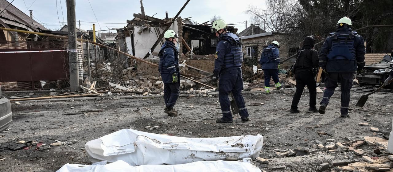 Body bags lie in front of a destroyed building.