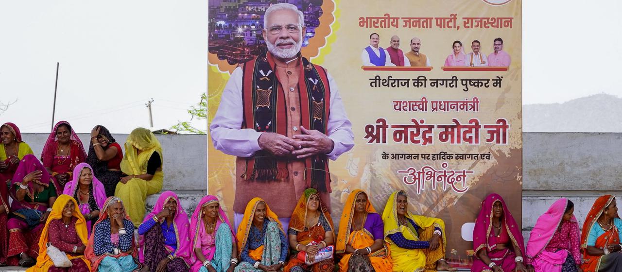 Frauen sitzen vor einem Wahlplakat von Narendra Modi.