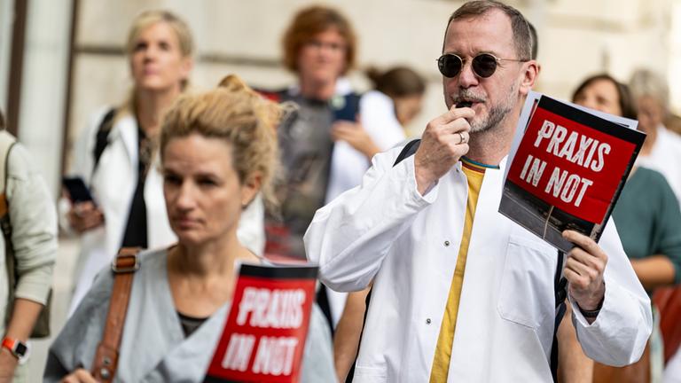 Ärzte gehen bei einem Protestmarsch mit Schildern mit der Aufschrift "Praxis in Not" durch Berlin Mitte.