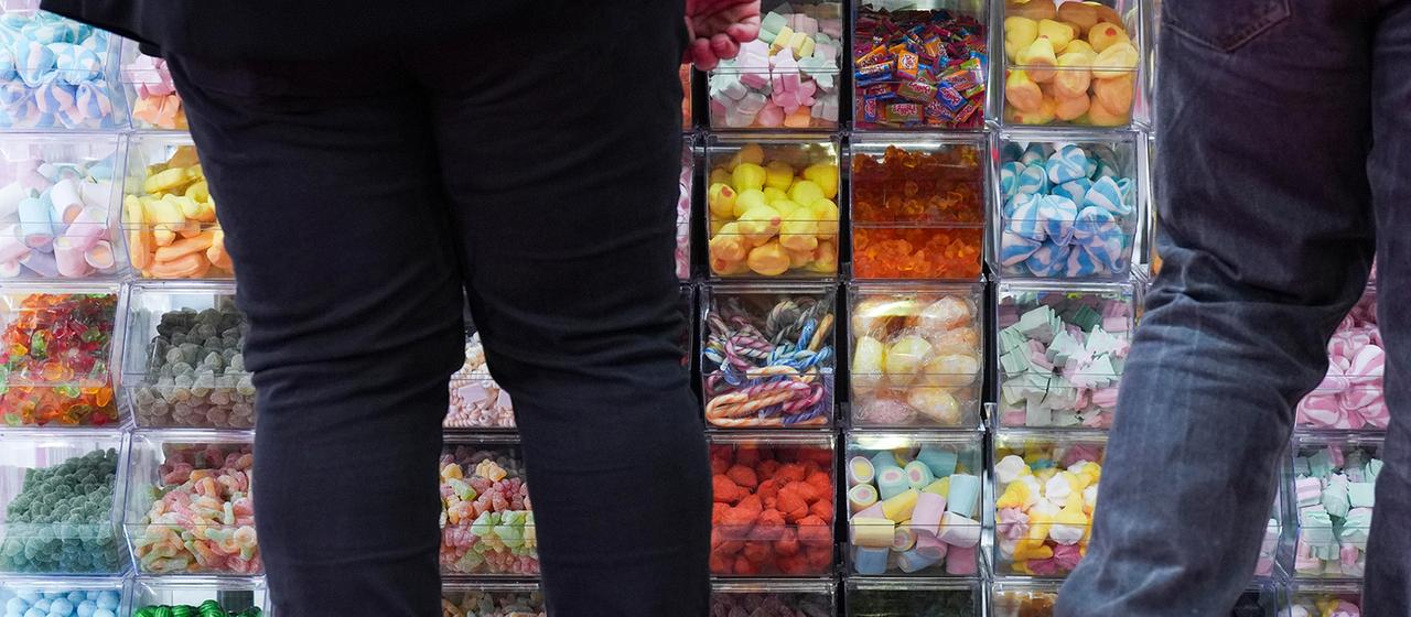 Kräftige Personen stehen vor einer Wand zur Selbstbedienug von Süssigkeiten.