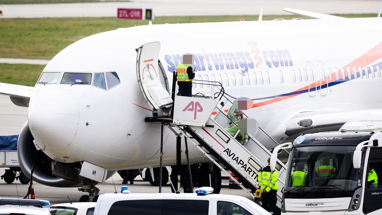 Zwei Frauen und ein Kind steigen neben einem Polizisten aus einem Flugzeug am Flughafen Hannover. 