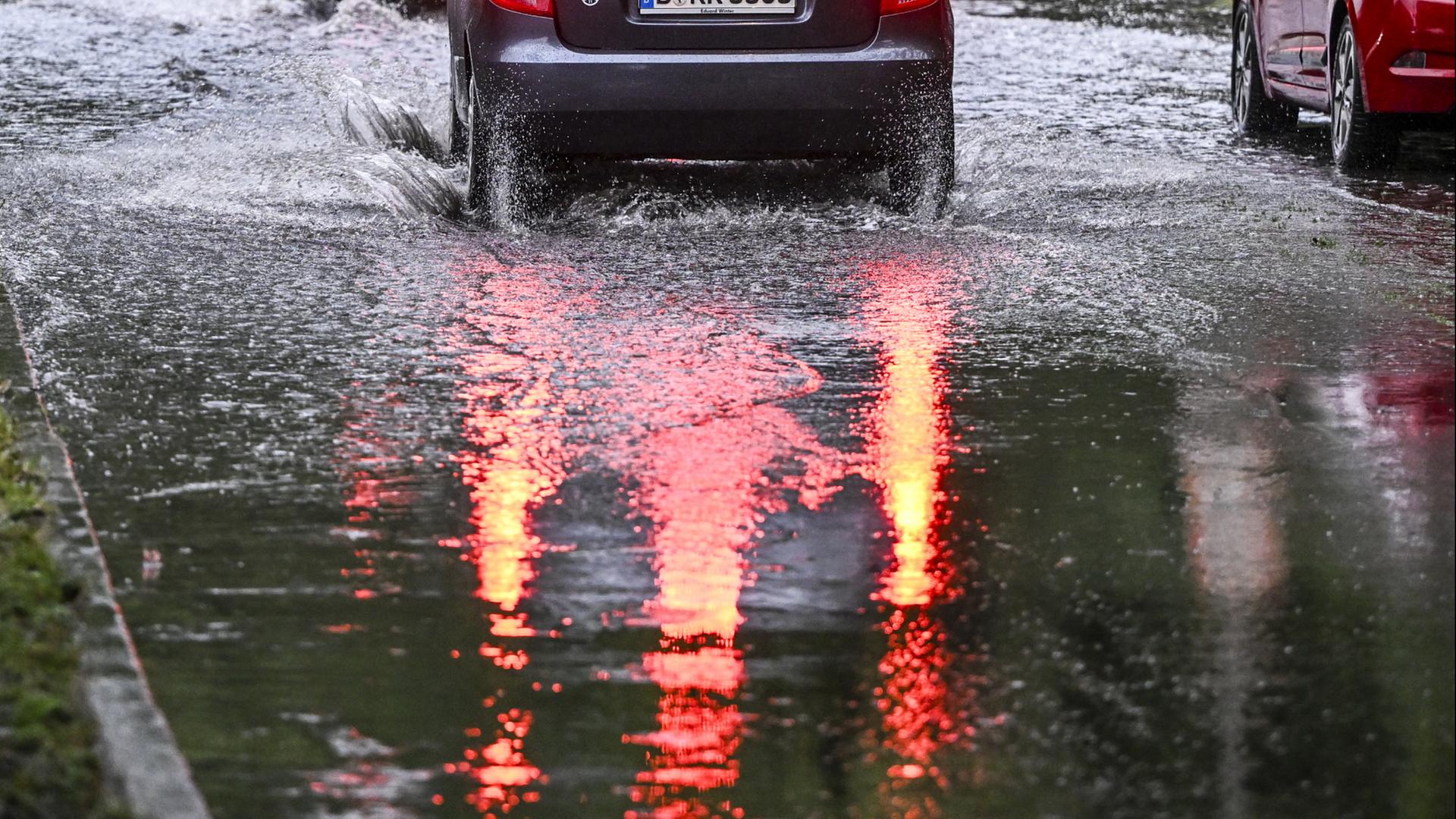 Nach starken Regenfällen fährt ein Auto in Berlin durch eine überspülte Straße | dpa