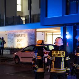 Im Bildvordergrund stehen drei Einsatzkräfte der Feuerwehr in dunkel-gelber Bekleidung und Helmen und blicken in Ricktung eines großen Wohnhauses. Im Bildhintergund unscharf weitere Einsatzkräfte und das Wohnhaus in der Dunkelheit.