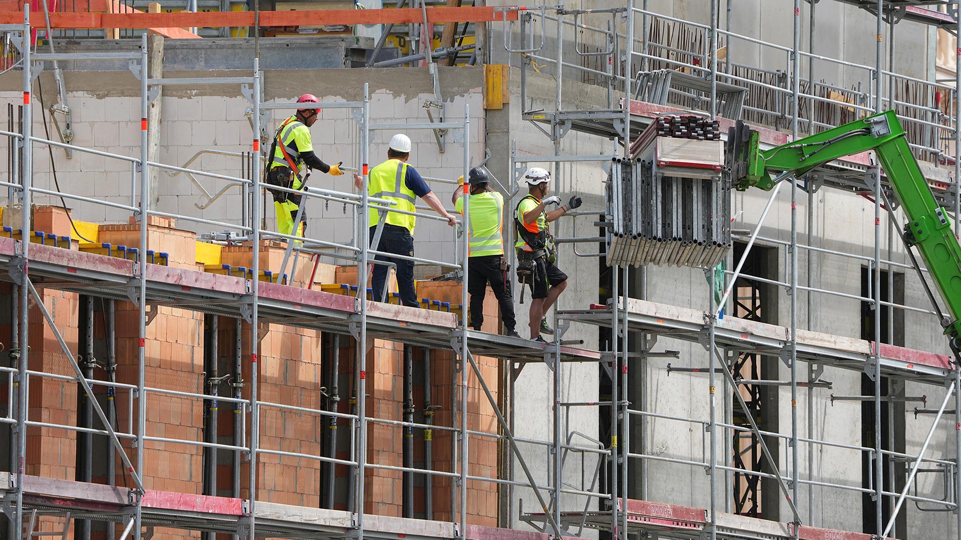 Vier Arbeiter stehen auf einem BaugerÃ¼st einer Baustelle. | picture alliance/dpa