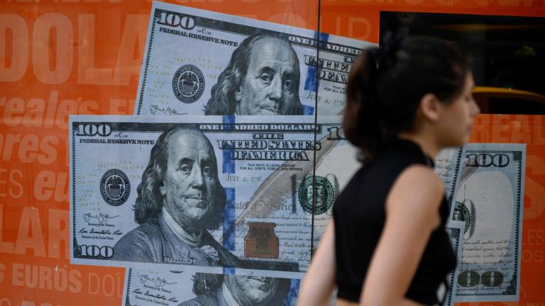 Eine Frau geht in Bunos Aires an einem Plakat mit Dollarscheinen vorbei.