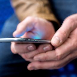 Ein junger Mann sitzt in einer S-Bahn und benutzt dabei sein Smartphone