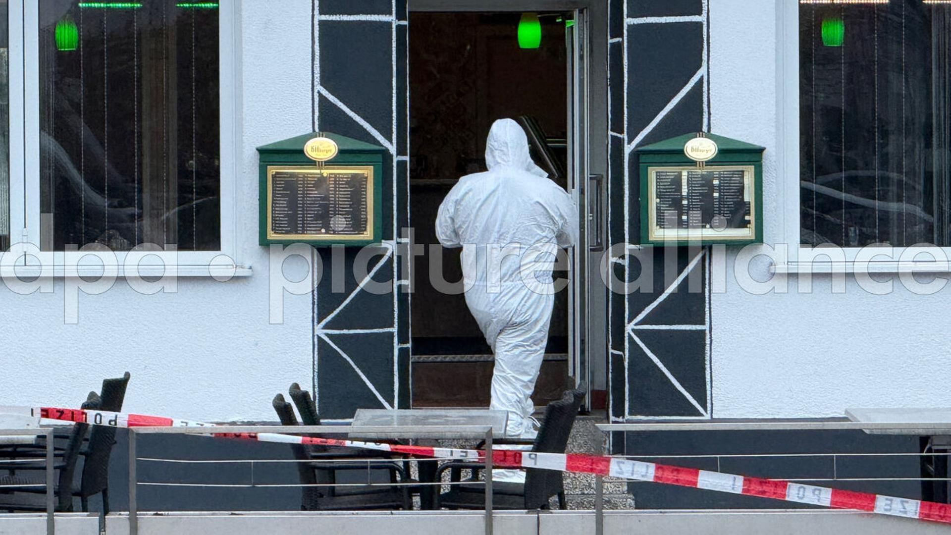 Ein Mann der Spurensicherung in weiÃem Kapuzenanzug vor dem Lokal in Raunheim, davor ein Absperrband der Polizei. | picture alliance/dpa/Mike Seeboth | Mike Seeboth