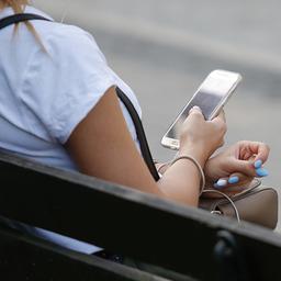 Eine junge Frau sitzt auf einer Bank und benutzt ihr Smartphone