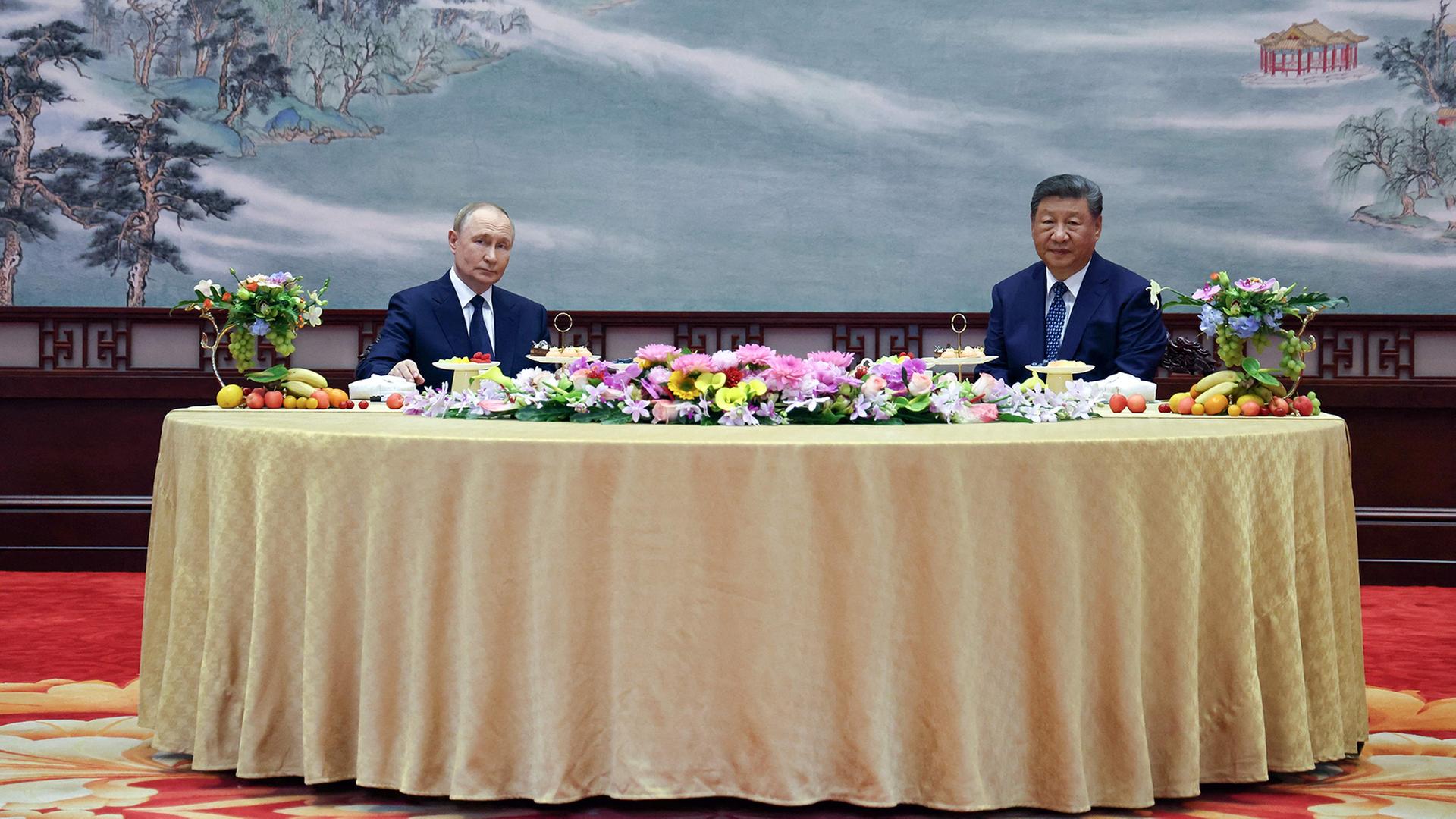 Wladimir Putin und Xi Jinping sitzen nebeneinander an einem Tisch. | AFP