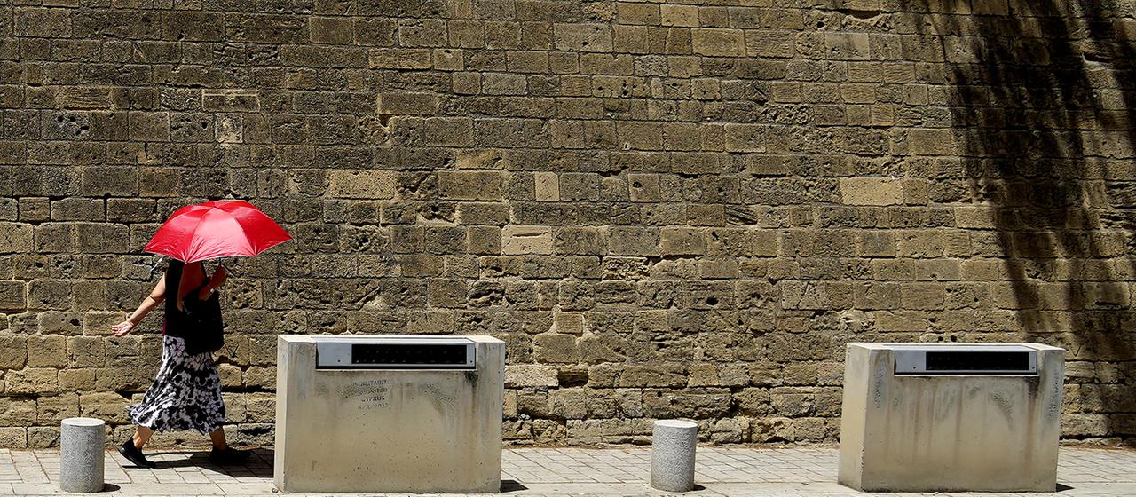 Eine Frau mit einem roten Schirm geht vor einer Mauer in Nikosia spazieren. | dpa Eine Frau mit einem roten Schirm geht vor einer Mauer in Nikosia spazieren.