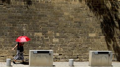 Eine Frau mit einem roten Schirm geht vor einer Mauer in Nikosia spazieren. 