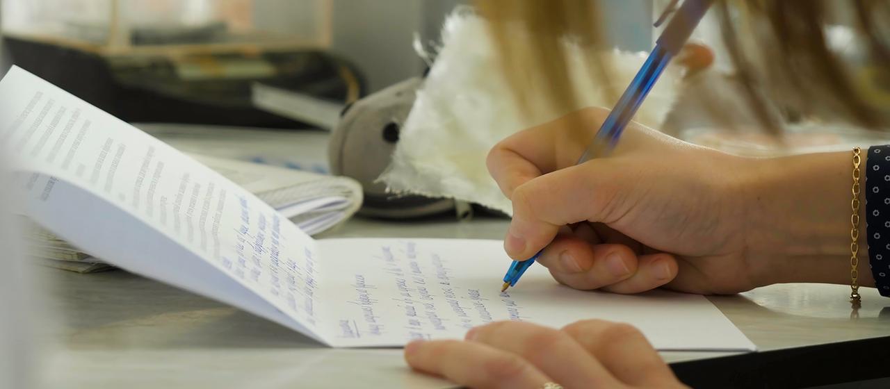 Nahaufnahme einer weiblichen Hand, die mit einem Stift auf ein Papier schreibt.