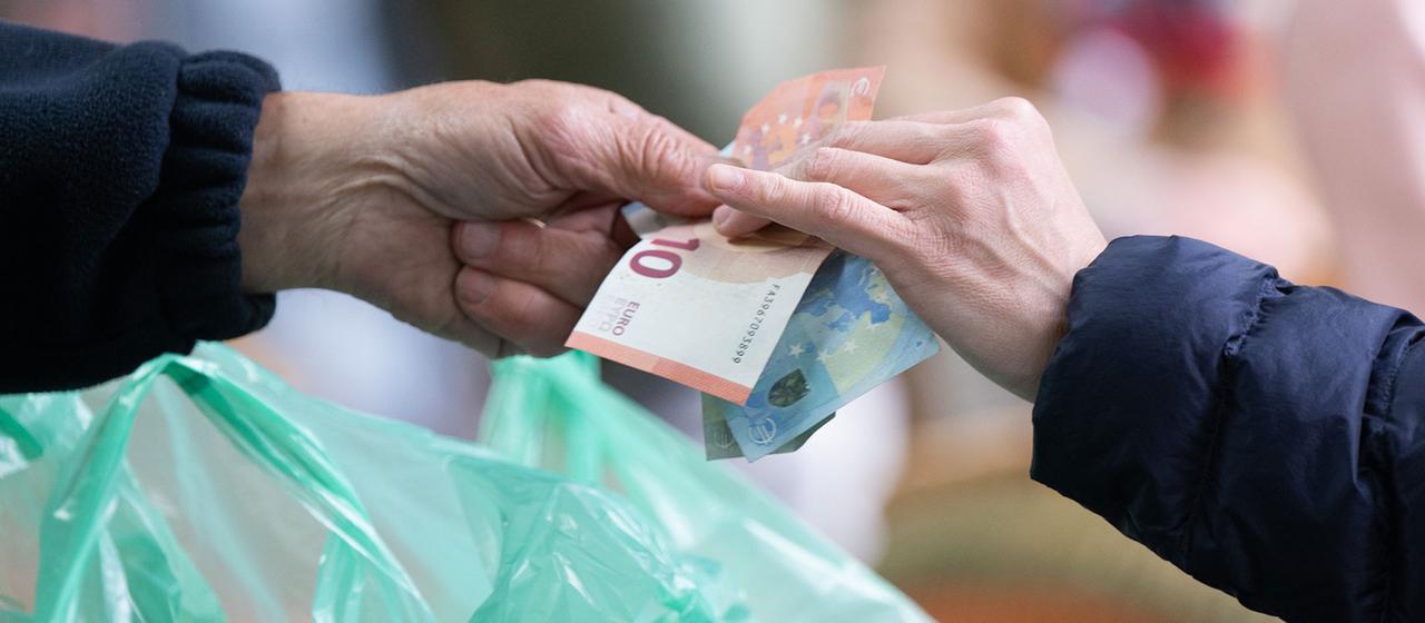 Eine Kundin bezahlt ihren Einkauf auf einem Wochenmarkt mit Bargeld.