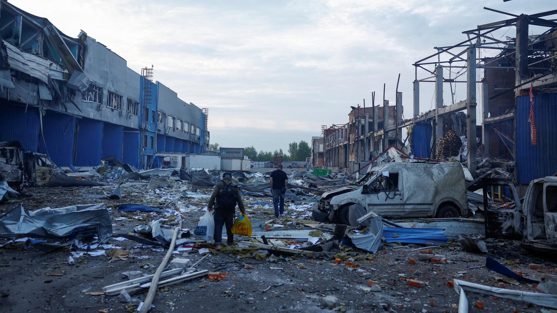 Menschen gehen in Kiew (Ukraine) zwischen Trümmern auf dem Gelände von Lebensmittel- und Getränkelagern. | REUTERS