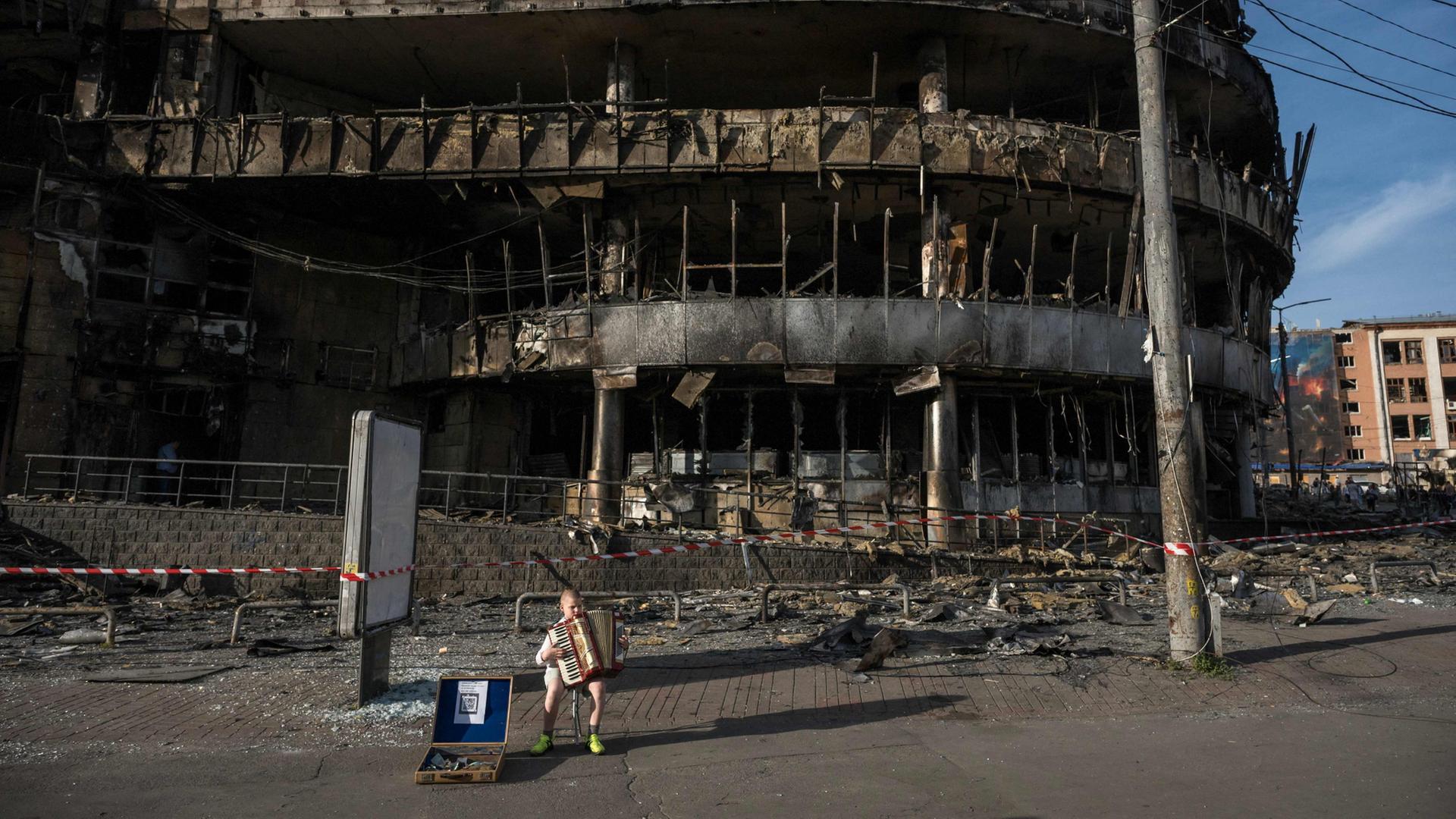 Ein Junge spielt vor einem beschädigten Einkaufszentrum Akkordeon. | AFP