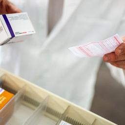 Ein Apotheker hält ein Medikament und ein Rezept in der Hand