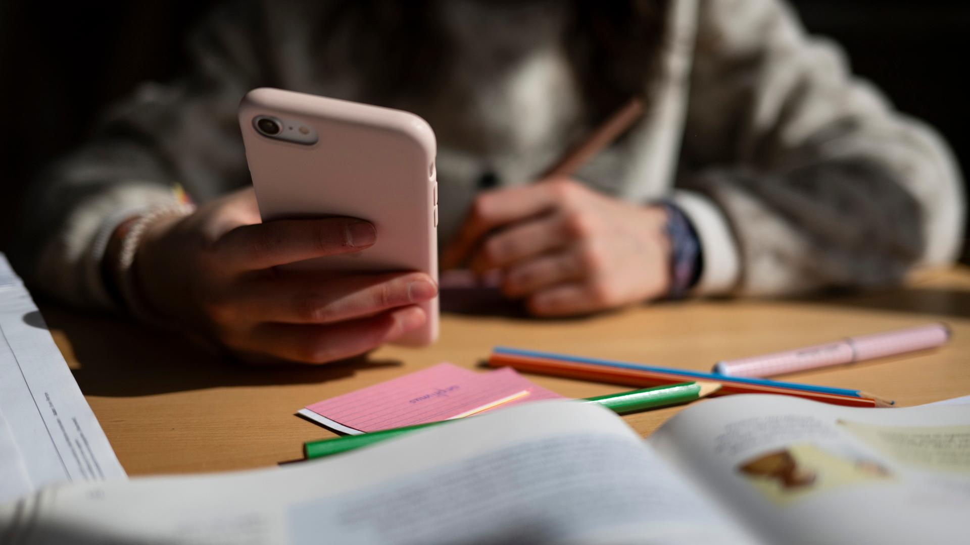 Ein Schulkind sitzt am Schreibtisch und h�lt ein Smartphone in der Hand. | picture alliance/dpa