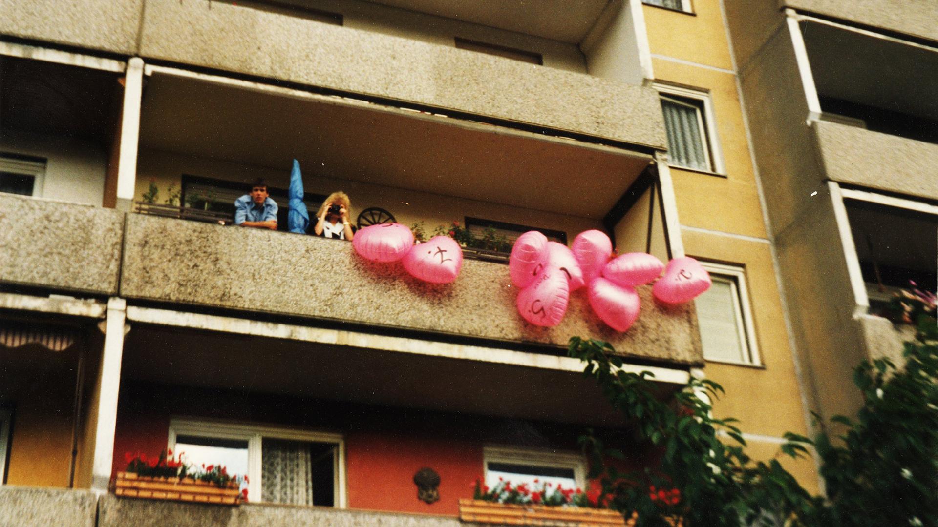 Luftballonherzen wehen in den 1990er Jahren an einem Balkon eines Plattenbaus im Wind. | Nadine Klaß