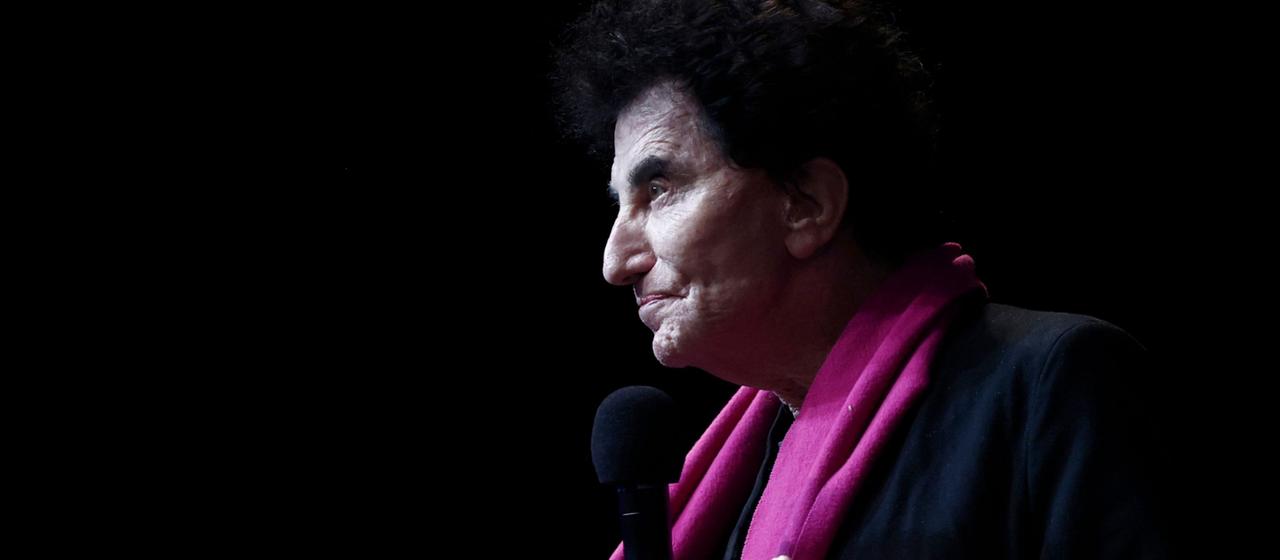 Jack Lang mit pinkem Schal und Mikrofon in der Hand