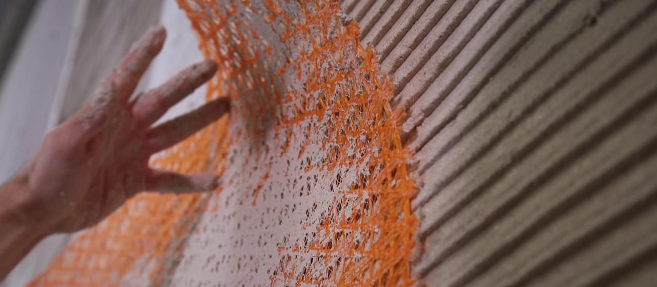 Un hombre fija una estera de fibra de vidrio a una pared.