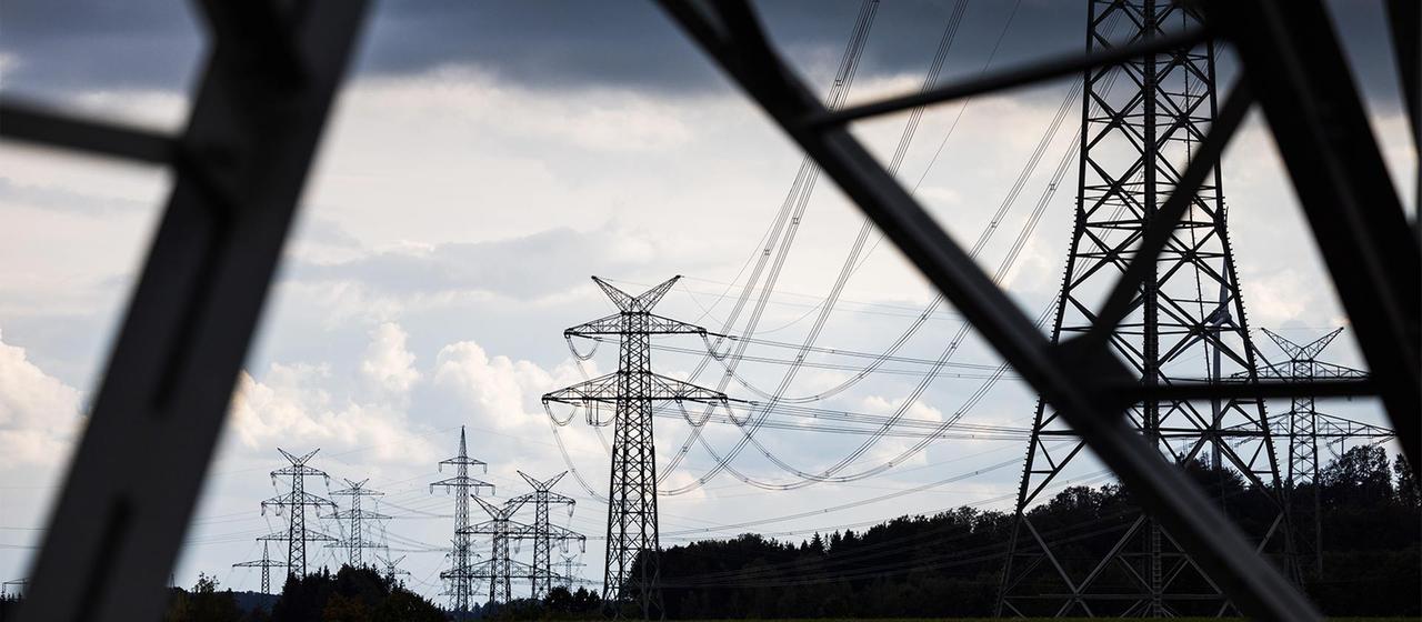 Strommasten einer Hochspannungsleitung unter dunklem Wolkenhimmel.