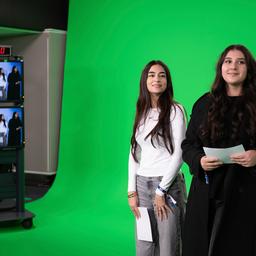 Zwei junge Frauen stehen in einem Fernsehstudio vor einer grünen Wand.
