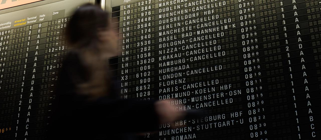 Eine Frau schaut beim Gehen auf eine Anzeigetafel mit annullierten Flügen am Frankfurter Flughafen. 