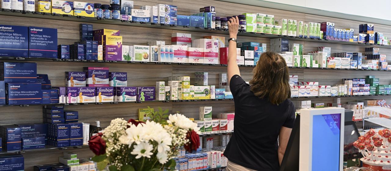 Eine Mitarbeiterin in einer Apotheke greift nach freiverkäuflichen Arzneimitteln.