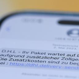 Auf einem Smartphone ist eine Betrugs-SMS zu lesen, in der Kriminelle ein Paket ankündigen und dafür Zollgebühren einfordern.