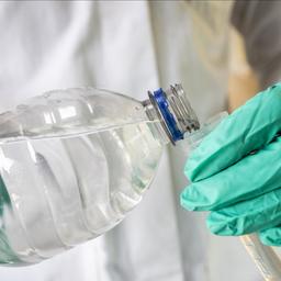 Hände mit Gummihandschuhen gießen eine Wasserprobe in ein Reagenzglas.