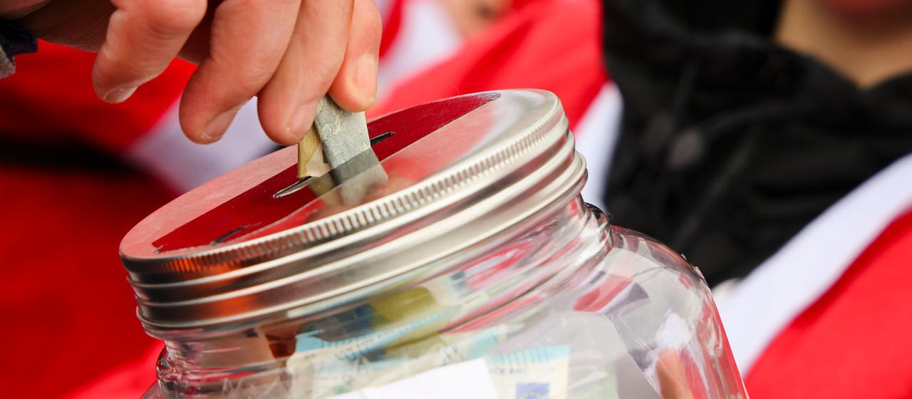 Ein Mann steckt einen Geldschein in ein Spendenglas.