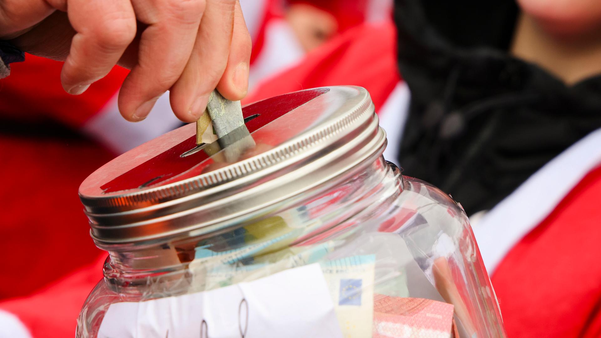 Ein Mann steckt einen Geldschein in ein Spendenglas. | picture alliance/dpa