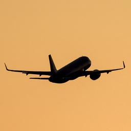 Ein Verkehrsflugzeug im Steigflug vor orangefarbenem Himmel.
