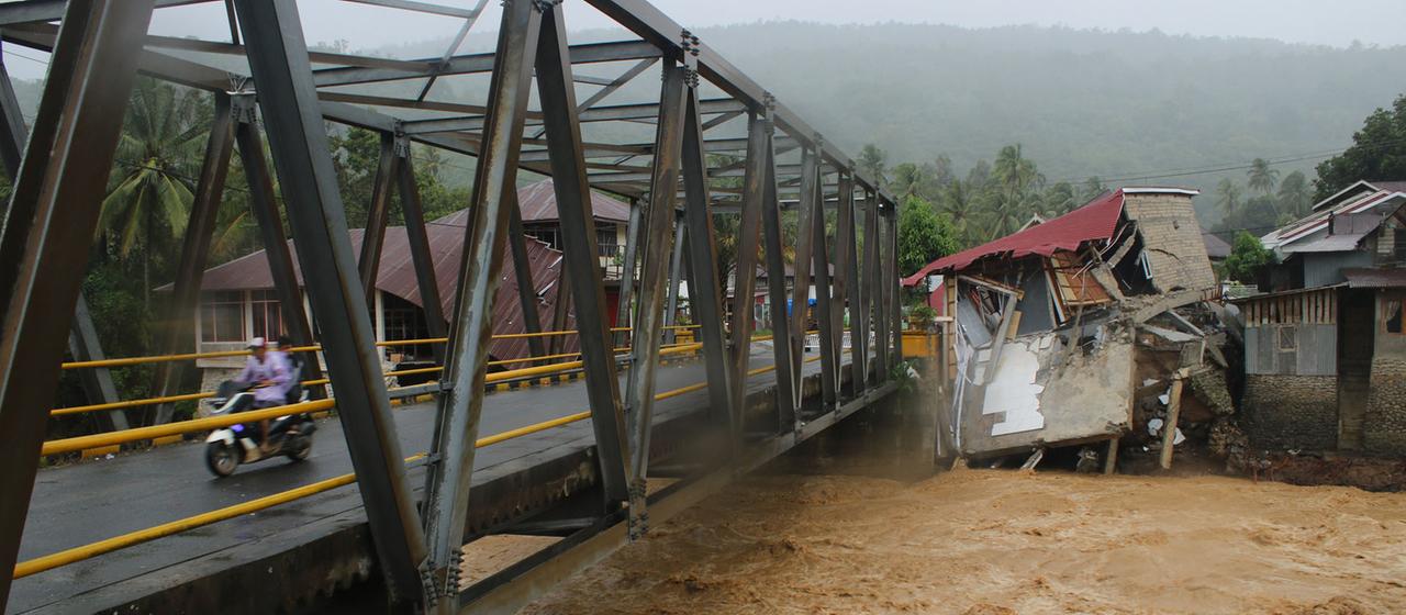 Autofahrer fahren auf einer Brücke vorbei an Gebäuden, die durch Überschwemmungen in Tanah Datar, West-Sumatra, Indonesien, beschädigt wurden. 