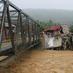 Autofahrer fahren auf einer Brücke vorbei an Gebäuden, die durch Überschwemmungen in Tanah Datar, West-Sumatra, Indonesien, beschädigt wurden. 