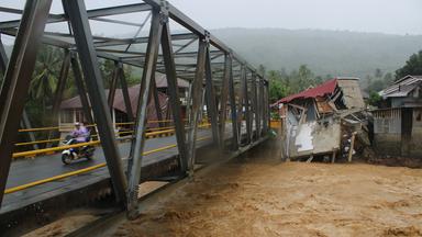 Autofahrer fahren auf einer Brücke vorbei an Gebäuden, die durch Überschwemmungen in Tanah Datar, West-Sumatra, Indonesien, beschädigt wurden. 